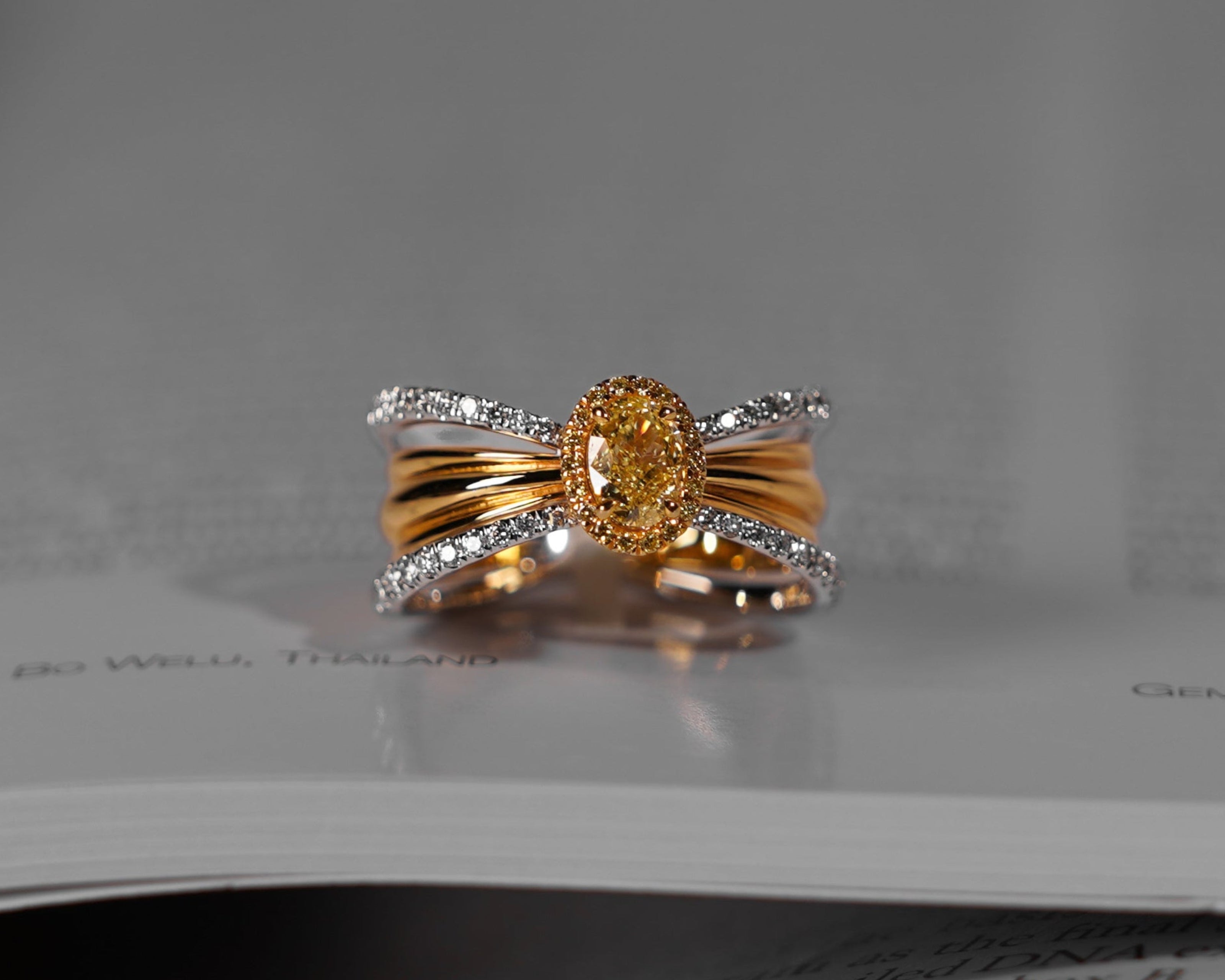 A gold and silver ring with a central oval yellow gemstone, resting on the pages of an open book.