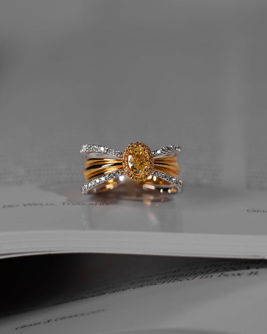 A gold and silver ring with a central oval yellow gemstone, resting on the pages of an open book.